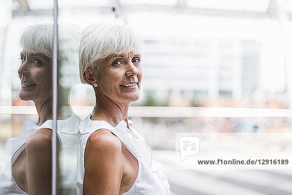 Portrait of smiling senior woman leaning against glass facade