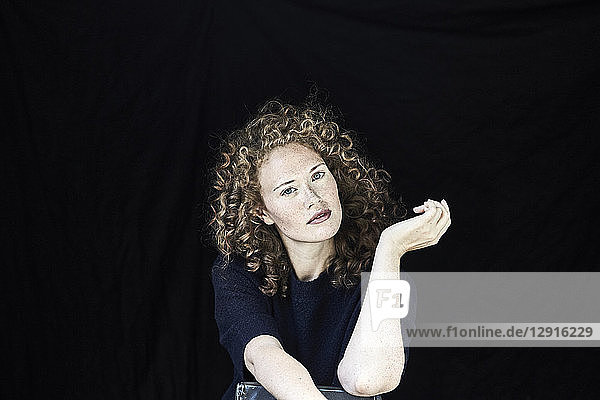 Portrait of young woman with curly hair in front of black background