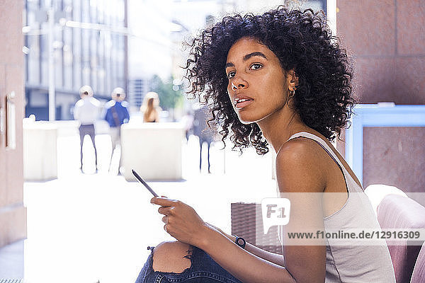Portrait of young woman with digital tablet sitting at sidewalk cafe watching something