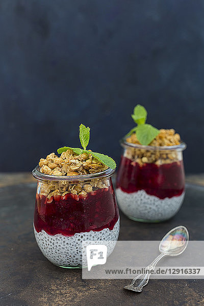Two glasses of chia pudding with coconut milk  red fruit jelly and peanut granola topping