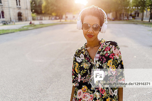 Fashionable young woman with sunglasses and headphones outdoors at sunset