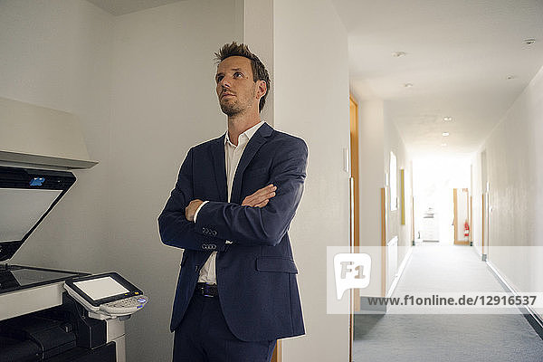 Bored businessman leaning against wall next to copying machine