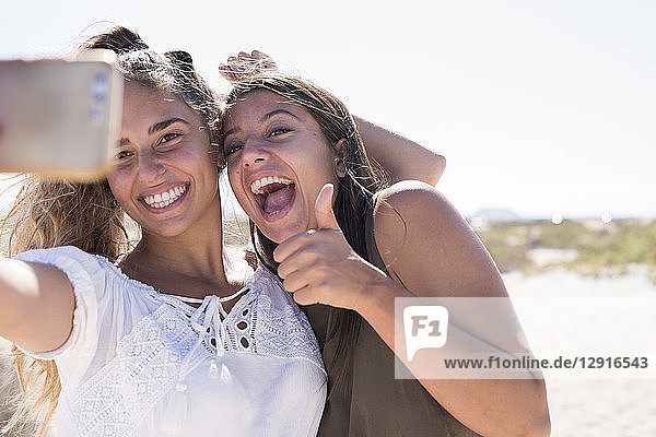 Girlfriends having fun on the beach  taking smartphone selfies