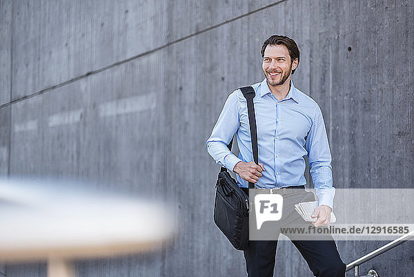 Portrait of smiling businessman with laptop bag at concrete wall