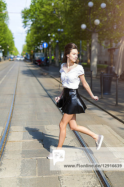 Young woman crossing a street with tramway tracks in the city