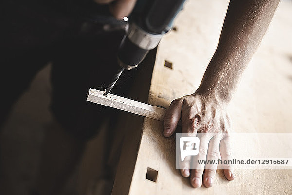 Close-up of carpenter using drill on piece of wood in workshop