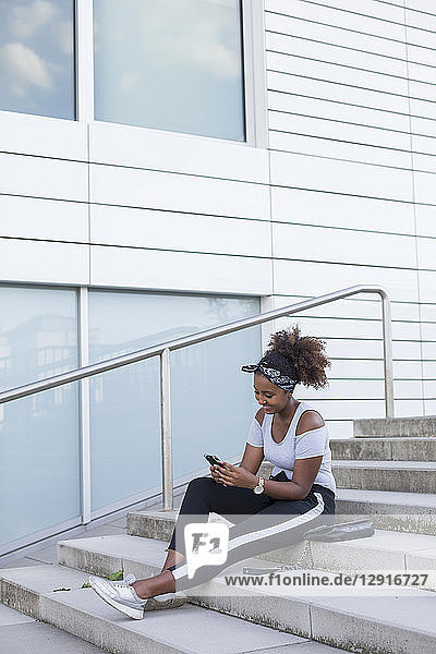Smiling young woman sitting on stairs looking at smartphone