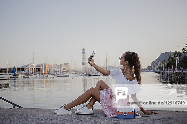 Fashionalble young woman sitting at the harbour of Barcelona  using smartphone
