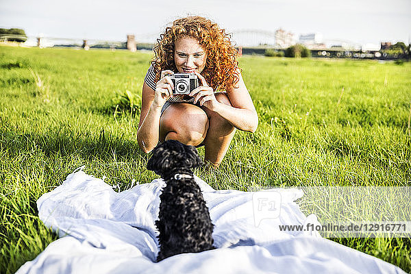 Germany  Cologne  portrait of smiling young woman on meadow taking picture of her dog