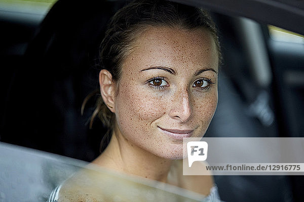 Portrait of freckled young woman looking out of car window