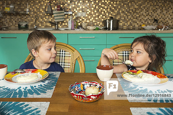 Portrait of boy and his little sister eating breakfast in the kitchen