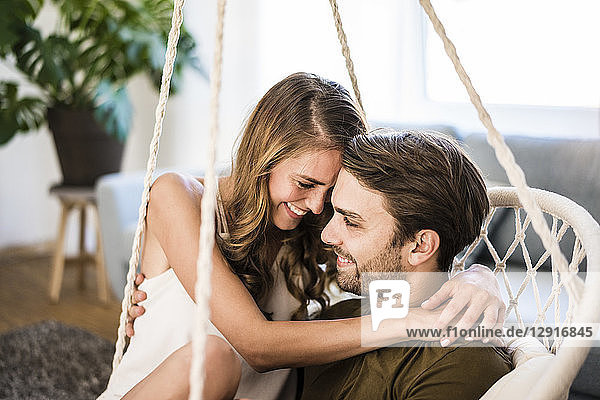 Happy affectionate couple embracing in hanging chair at home