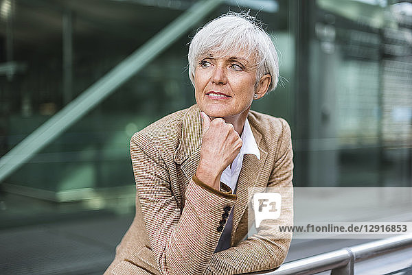 Portrait of senior businesswoman leaning on railing in the city looking around