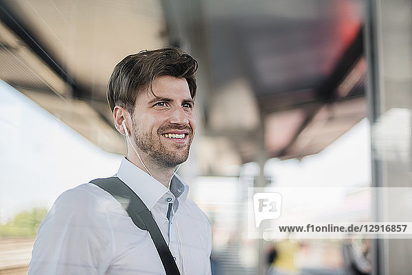 Portrait of smiling businessman on station platform with earphones