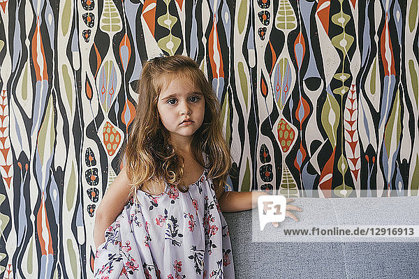 Portrait of serious little girl on couch in front of patterned wallpaper
