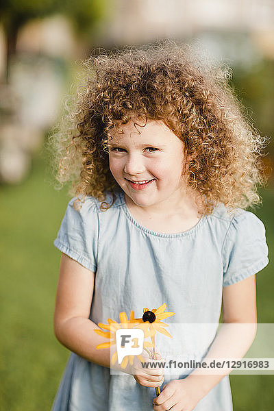 Portrait of happy little girl with picked flowers in the garden