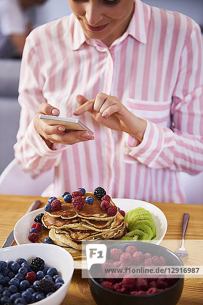 Young woman using smartphone at breakfast