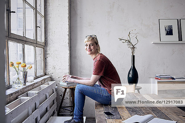 Portrait of smiling woman with coffee mug sitting on desk in loft