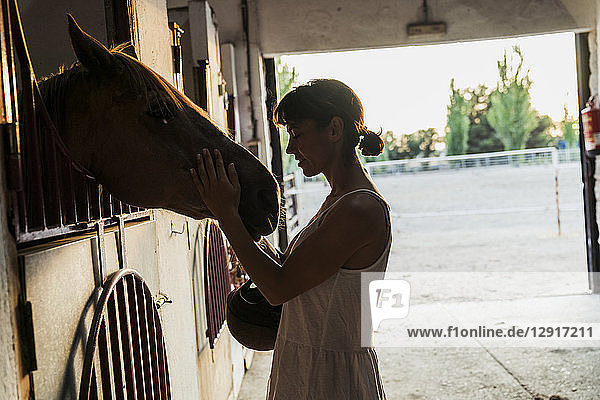 Woman stroking horse in stable