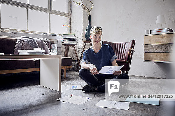 Smiling woman sitting on the floor in a loft looking at papers