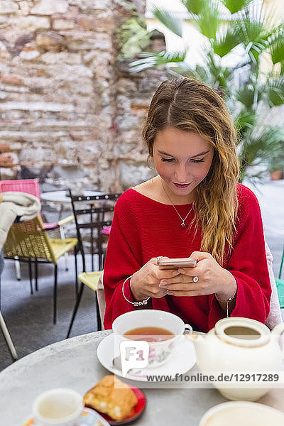 Young woman sitting at pavement cafe using smartphone