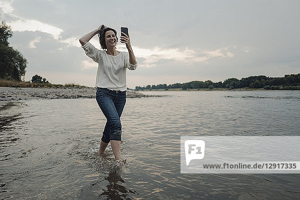 Laughing woman running at the riverside  taking selfies