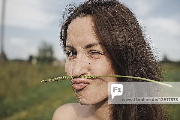 Portrait of woman balancing plant stalk on her mouth twinkling