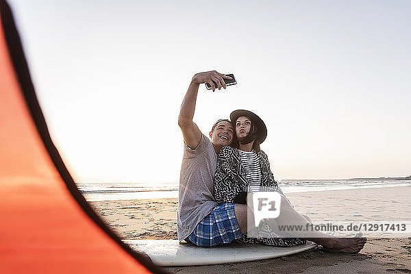Couple camping on the beach  taking smartphone selfies