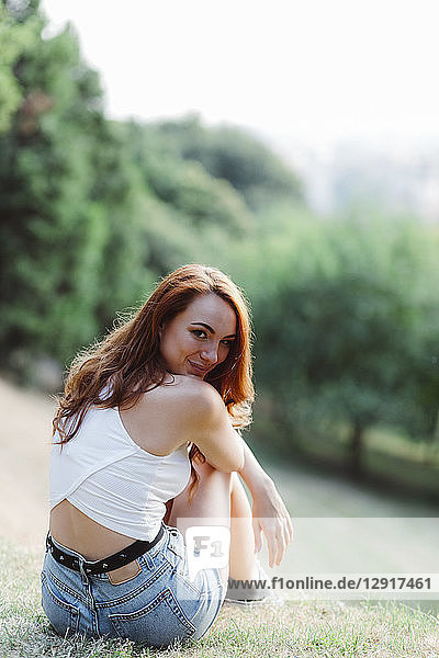 Smiling redheaded woman relaxing on hill in a park