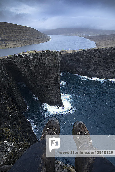 Personal perspective shot with feet of person sitting on edge of coastal cliff  Sorvagsvatn  Faroe Islands