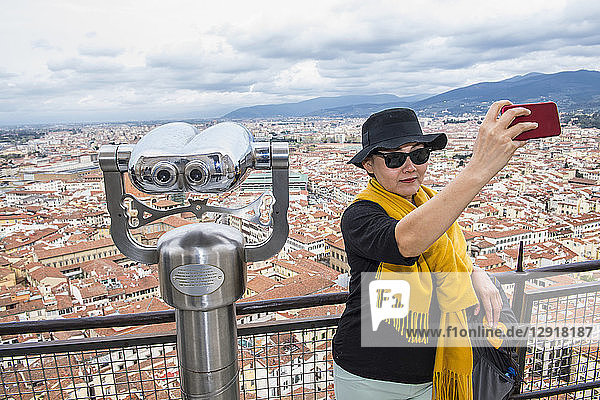 Ältere Frau  die ein Selfie neben einem münzbetriebenen Fernglas auf der Spitze einer Kathedrale macht  Florenz  Toskana  Italien