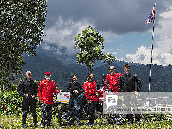 Gruppe von Freunden  die zusammen neben einem Motorrad posieren  mit einem bewaldeten Hügel im Hintergrund  Nan ¬ÝMueang¬ÝChiang¬ÝRai¬ÝDistrikt  Thailand