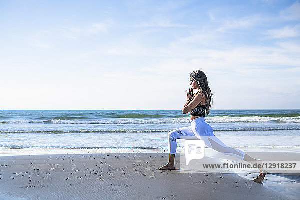 Side view shot of young woman with black hair doing yoga on beach