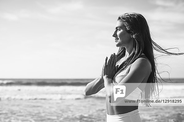 Side view photograph of young woman doing yoga on beach