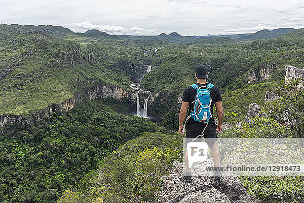 Junger Erwachsener steht auf einem Felsvorsprung mit schöner Cerrado-Naturlandschaft im Hintergrund  Mirante da Janela-Wanderung  Chapada dos Veadeiros  Goias  Zentralbrasilien