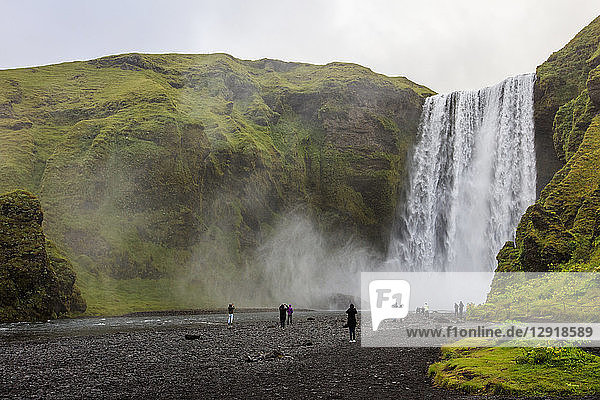 Touristen besuchen den Skogafoss  einen der berühmtesten Wasserfälle in Island. Der Wasserfall liegt in der NÃ?he des Highway One (auch als RingstraÃŸe bekannt) und stÃ?rzt sich 60 Meter in die Tiefe  und es gibt Pfade  die es Besuchern ermÃ¶glichen  bis zum FuÃŸ und zur Spitze des Wasserfalls zu gehen. Der Wasserfall befindet sich am Fluss Skoga  der durch das isländische Hochland fließt  bevor er den Atlantik erreicht.