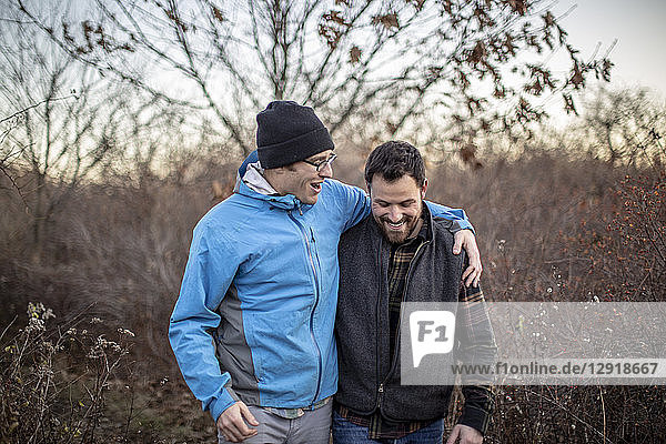 Zwei männliche Freunde lachen und unterhalten sich bei einem Spaziergang durch Grasland  Peaks Island  Maine  USA