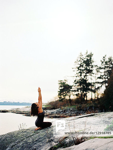 Seitenansicht einer Frau mit schwarzen Haaren beim Yoga am Meer