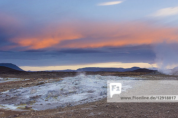 Ein blau gefärbtes  kochend heißes Schlammbecken stößt Dampf aus  während der Sonnenuntergang den Himmel orange färbt  im Hverarˆšˆ'ndor Hverir Geothermalgebiet am Namaskard-Pass  Nordisland.