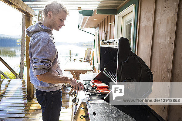 Side view of man cooking sausages on barbecue grill