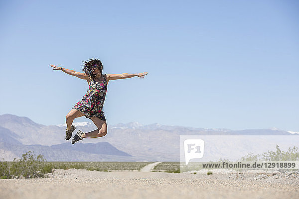 Erwachsene Frau im Kleid springt auf abgelegener Straße im Death Valley National Park in die Luft  Death Valley  Kalifornien  USA