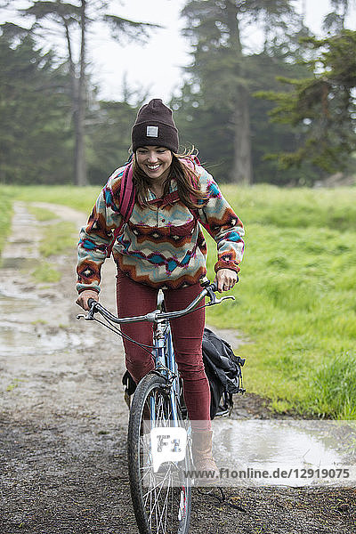 Young adult woman riding on bike through grassy area towing small trailer   Santa Cruz  California  USA