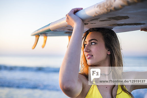 Kopf- und Schulteraufnahme einer Frau im gelben Bikini mit Surfbrett