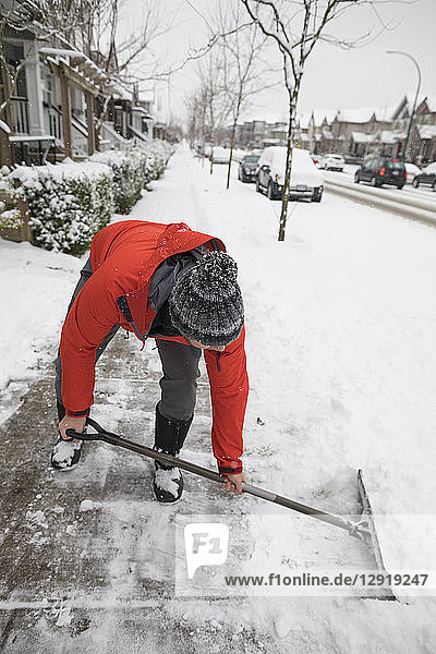 Totale Aufnahme eines Mannes  der im Winter in einem Vorort den Schnee vom Bürgersteig schaufelt