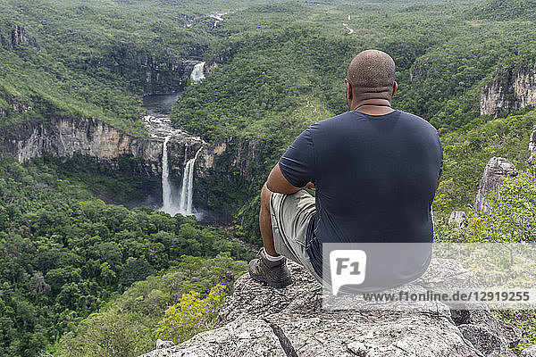 Mittlerer erwachsener Mann  der auf einem Felsen sitzt  mit schöner Cerrado-Landschaft im Hintergrund  Mirante da Janela Wanderung  Chapada dos Veadeiros  Goias  Zentralbrasilien