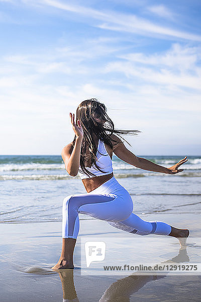 Junge Frau mit schwarzen Haaren macht Yoga am Strand