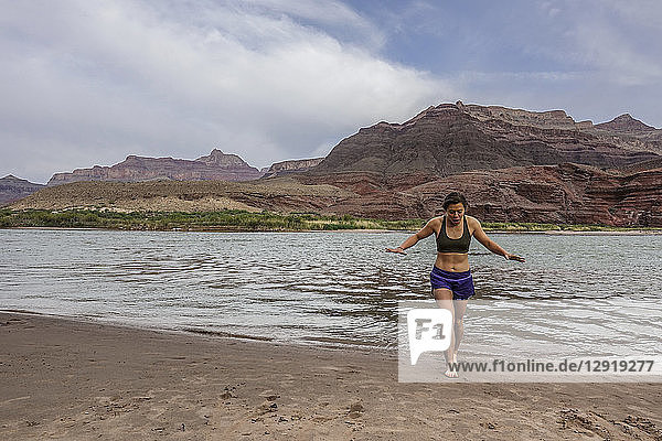 Young woman emerges from cold water of Colorado River after cooling off her feet to celebrate end of long day of hiking  Grand Canyon  Arizona  USA