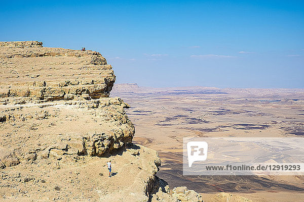 Distant view shot of hiker standing near edge of Makhtesh Ramon Crater  Negev Desert  Mitzpe Ramon  Southern District  Israel