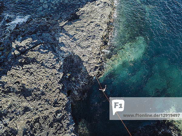 Aerial view of young shirtless man balancing across tightrope over coastal water ¬ÝTenerife Canary Islands Spain