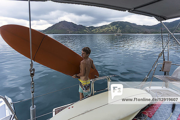 Three quarter length shot of young man carrying surfboard on yacht